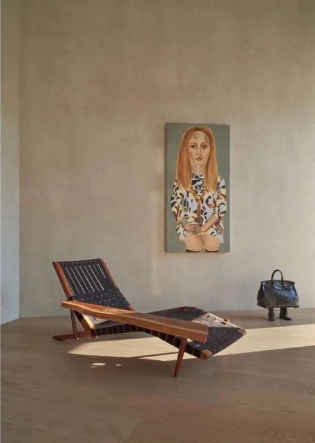 Modern interior showcasing a wooden lounge chair, painting of a woman, and a handbag with legs in a neutral colour palette.