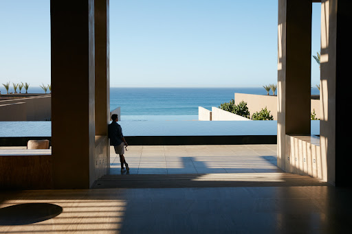 Man leaning against a column overlooking the ocean. Exterior architecture and design featuring an infinity pool and turquoise water.
