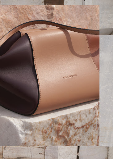 Fashion product shot of a two-tone leather handbag on a marble block background, highlighting neutral colors and minimalist design.