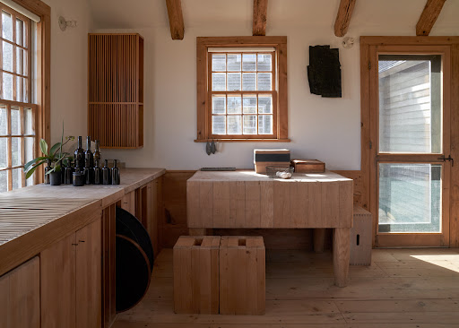Sunlit kitchen interior featuring light wood cabinetry, a central island, and a collection of black vases on the counter.