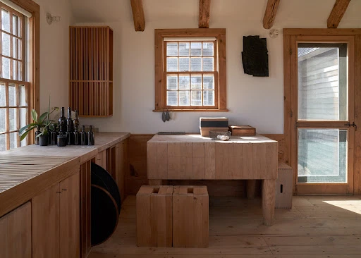 Sunlit kitchen interior featuring light wood cabinetry, a central island, and a collection of black vases on the counter.