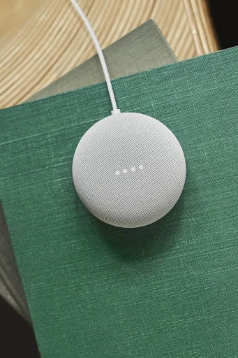 Smart home device on stacked green and tan books. Close-up shot of a Google Nest Mini on top of books in an indoor setting.