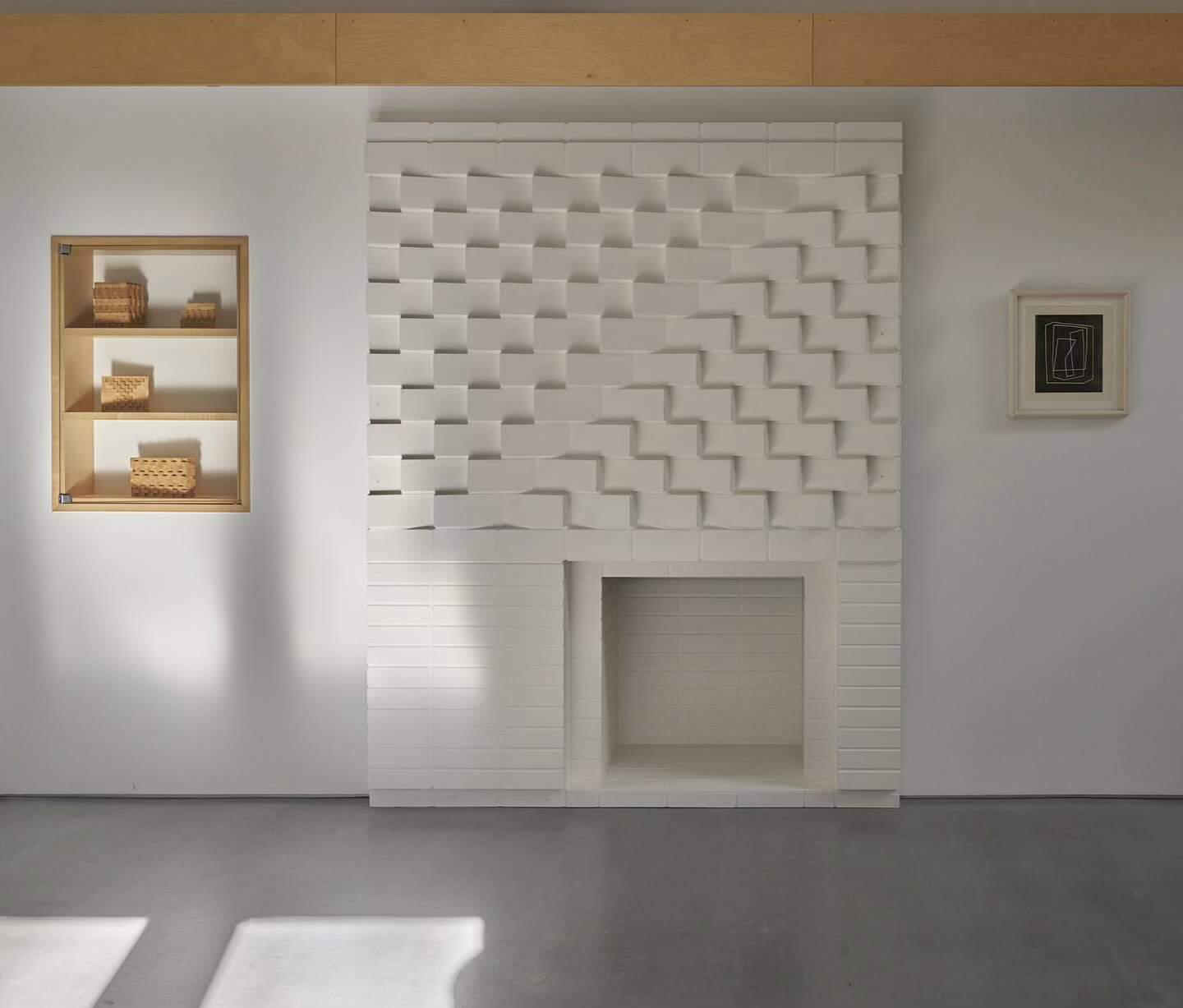 Minimalist interior featuring a custom white fireplace with a geometric design, recessed shelving, and decorative baskets.