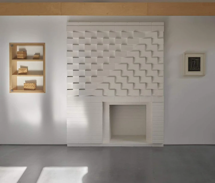 Minimalist interior featuring a custom white fireplace with a geometric design, recessed shelving, and decorative baskets.
