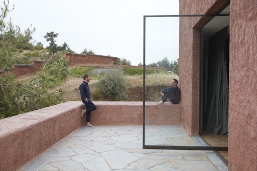 Two men standing and sitting on a terracotta terrace overlooking a green hillside, photographed by Martien Mulder