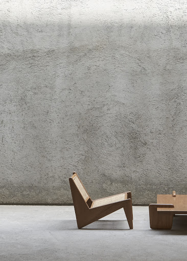 Modern wooden lounge chair with woven cane seat against a textured grey concrete wall by Martien Mulder