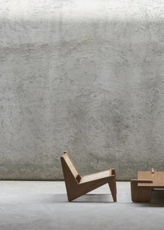 Modern wooden lounge chair with woven cane seat against a textured grey concrete wall by Martien Mulder