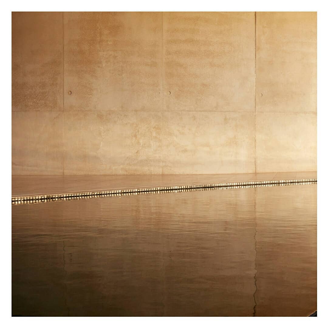 Minimalist interior featuring a reflective pool, seamlessly integrating with a textured beige wall, creating a serene and architectural space.