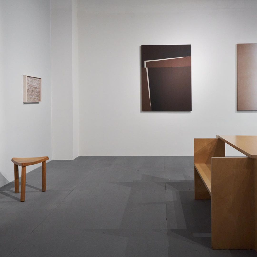 Minimalist art gallery interior featuring geometric abstract paintings in shades of brown and gray with wooden furniture. Modern aesthetic.