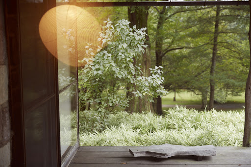 View from a porch onto a verdant garden with sunlight filtering through the trees, creating a tranquil and inviting outdoor scene.