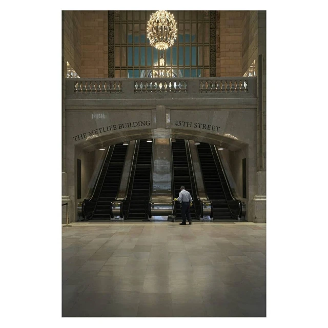 Interior view of a train station with escalators, featuring a maintenance worker and architectural details, including a chandelier and signage.