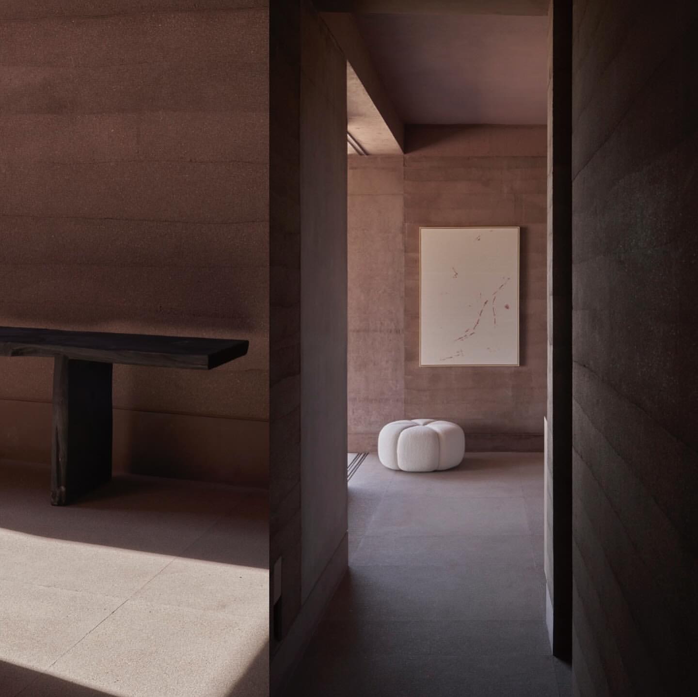Minimalist interior featuring an earth-toned textured wall, dark wood bench, white pouf, and neutral artwork, showcasing modern interior design.
