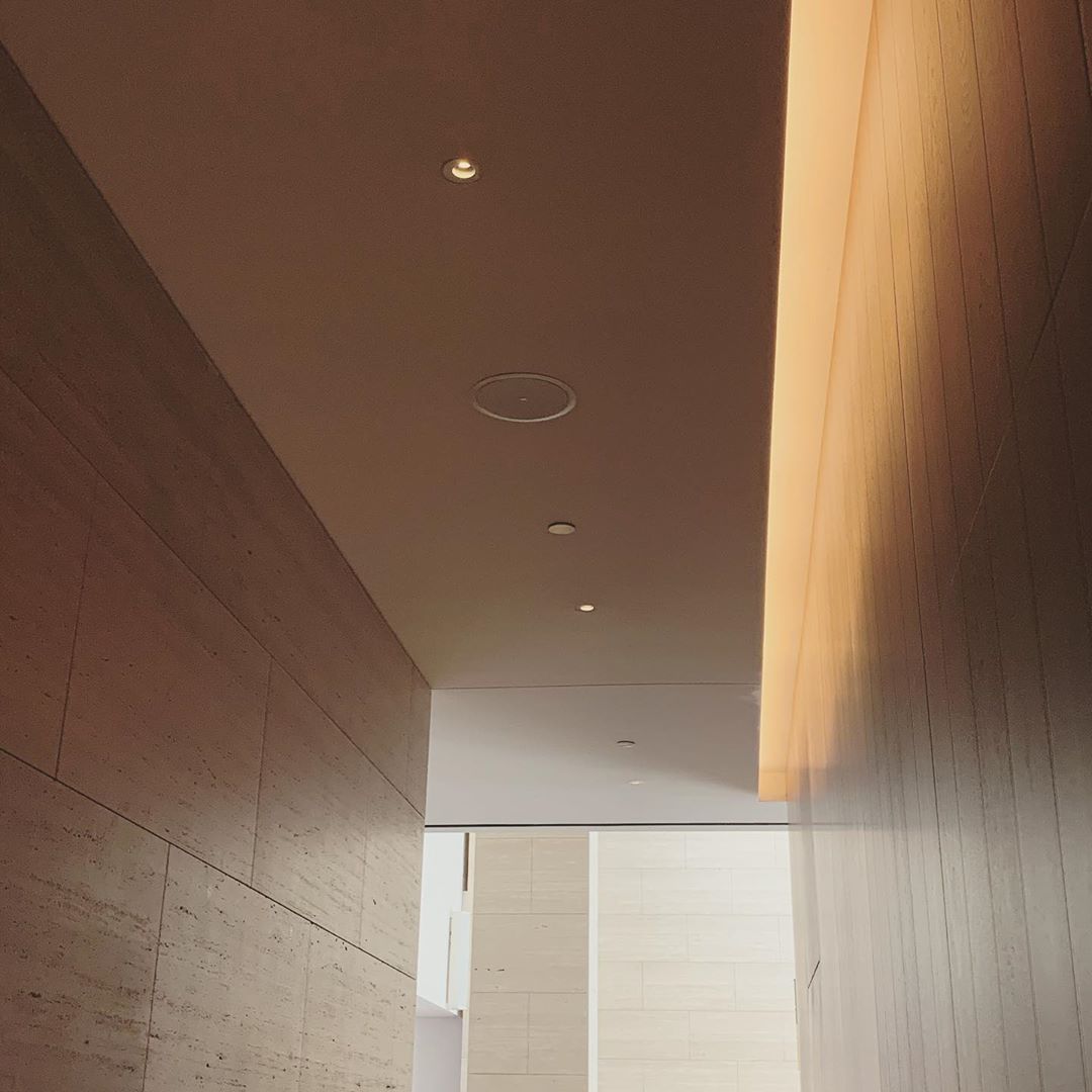 Interior view of an indoor hallway featuring a white ceiling with recessed lighting and beige walls, suggesting a modern architectural style.