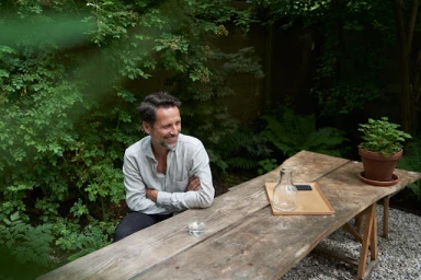 Man seated at a rustic wooden outdoor table in a lush garden by Martien Mulder