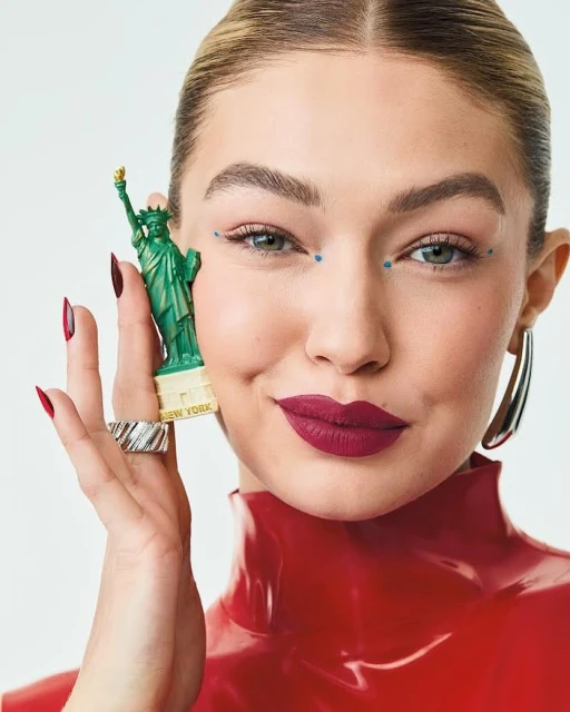 Close-up studio shot of a woman in red holding a miniature Statue of Liberty, showcasing beauty makeup and fashion accessories.