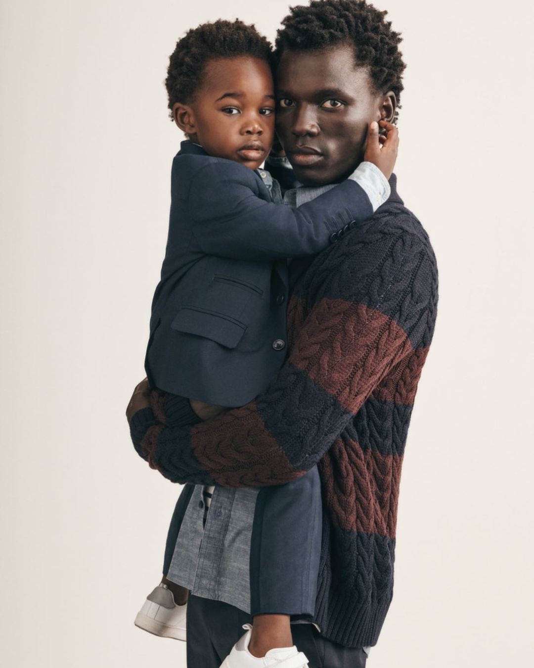 Father and son in a fashion studio, the father is holding his child, both are wearing stylish clothing, in a portrait studio.