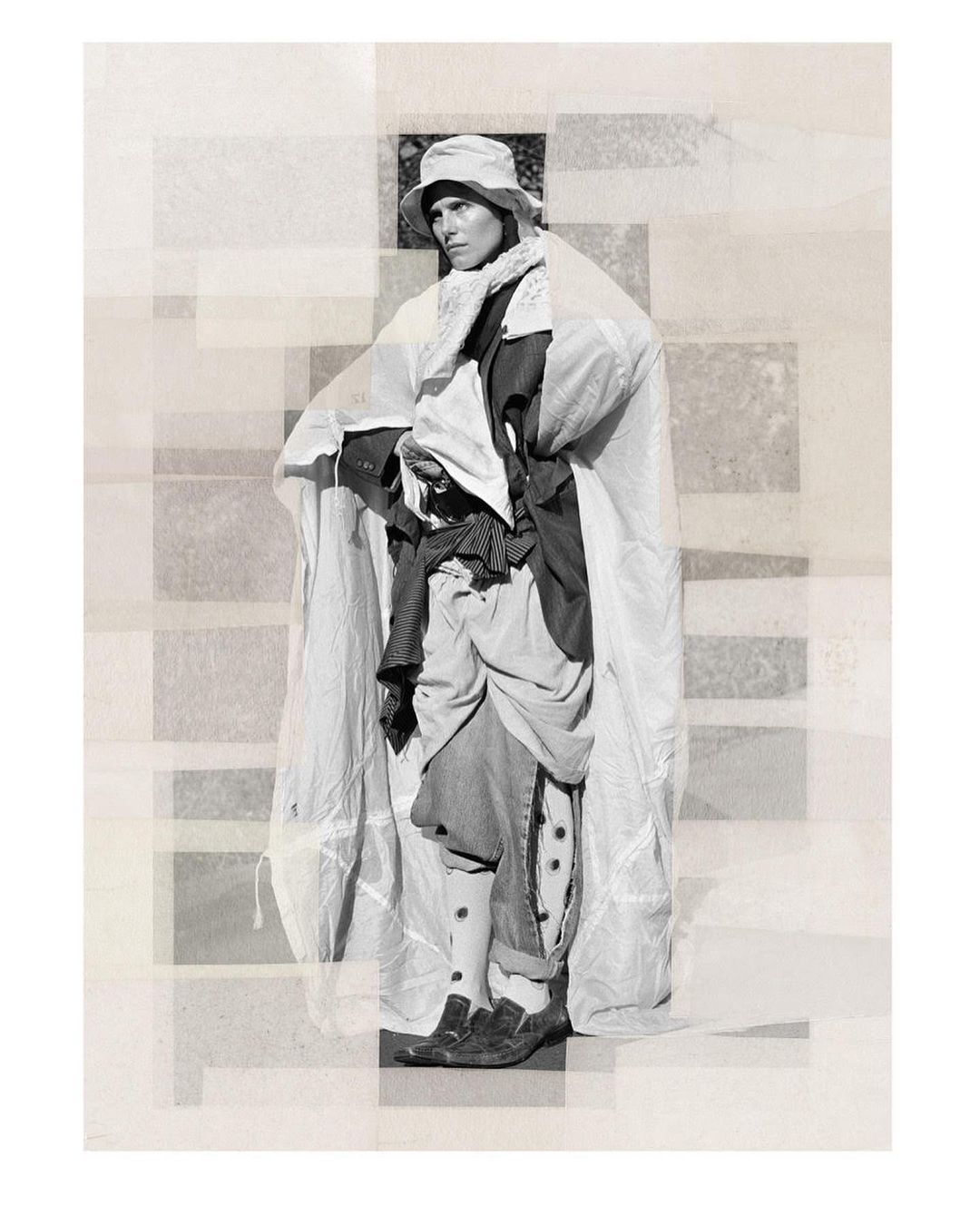 Monochrome fashion shot of a person wearing a bucket hat and draped in white fabric, standing against a geometric backdrop.