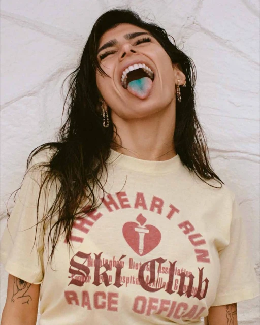 Young woman with open mouth and blue tongue shows off vintage t-shirt with heart design. Indoor shot against textured wall.