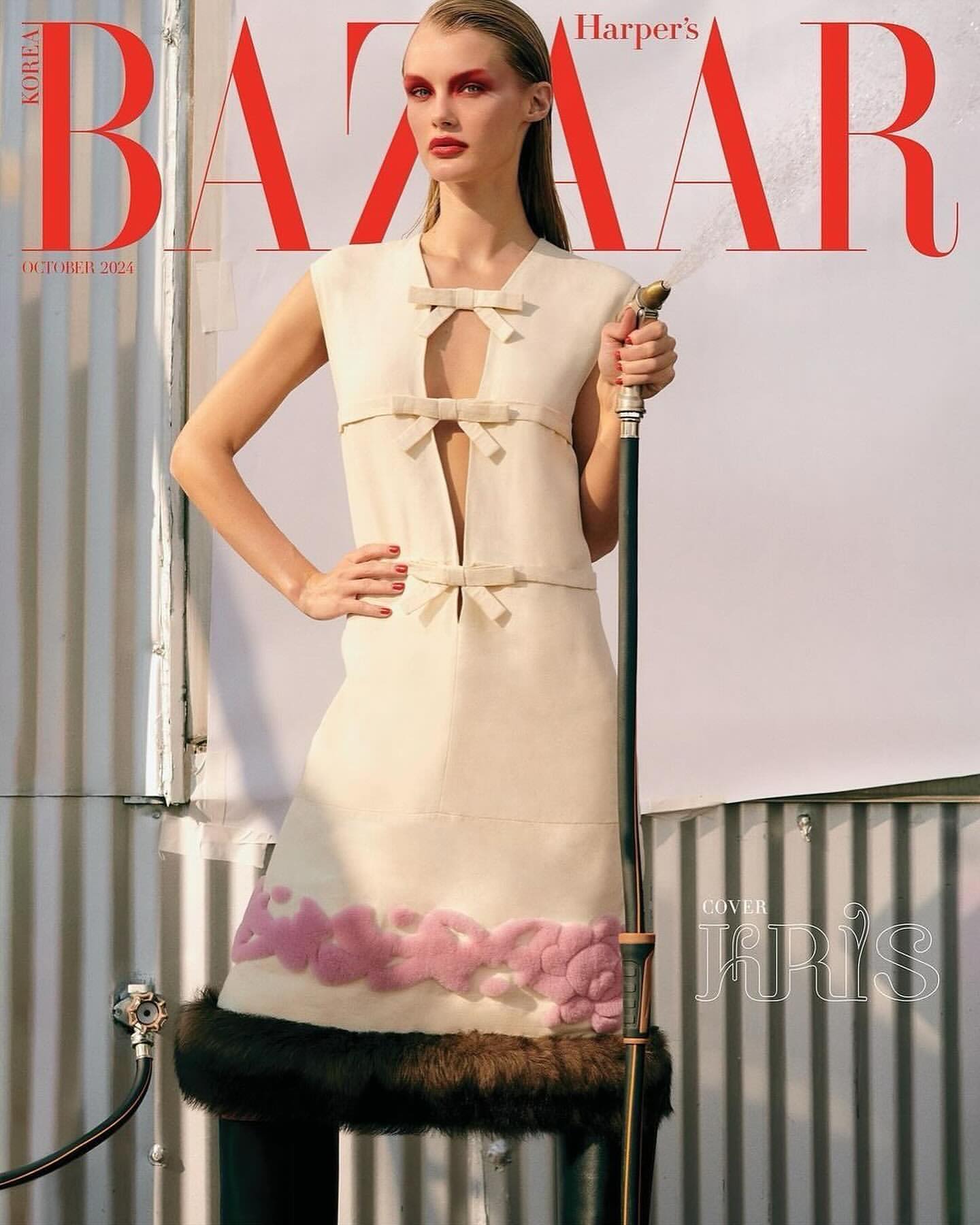 Harper's Bazaar cover featuring a blonde model in a cream dress with pink accents, holding a garden hose, set against a corrugated metal backdrop.