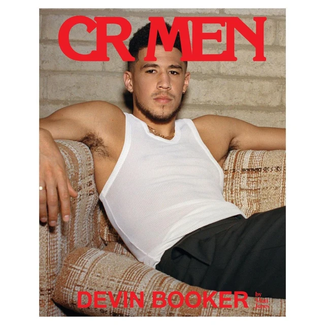 Devin Booker cover CR Men magazine with indoor shot of him sitting wearing a white tank top and dark pants on patterned couch.