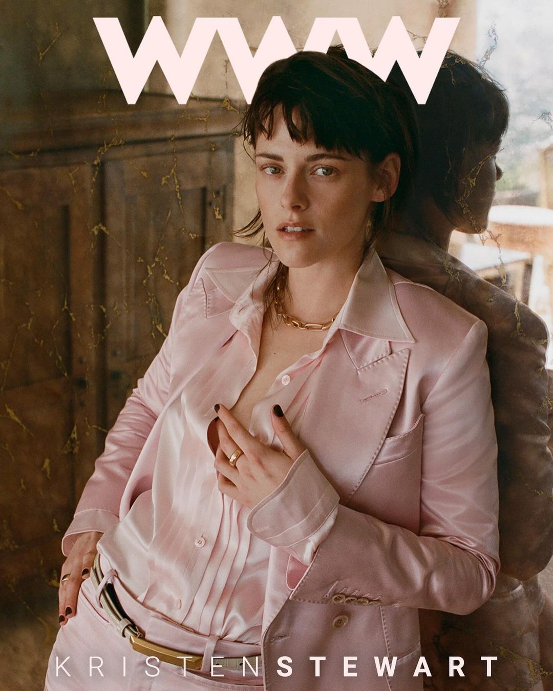 Kristen Stewart wears a pink suit and gold chain with a blurred mirror reflection on a magazine cover with large pink 'W' logo.