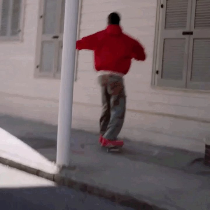 Person in a red jacket skateboarding on a concrete sidewalk next to a white building with windows, showcasing an outdoor urban activity.