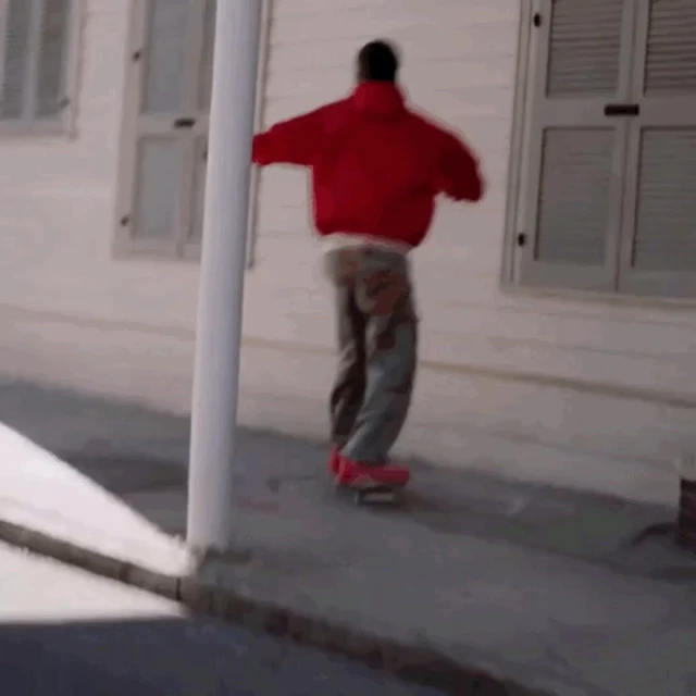 Person in a red jacket skateboarding on a concrete sidewalk next to a white building with windows, showcasing an outdoor urban activity.