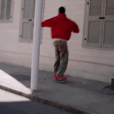 Person in a red jacket skateboarding on a concrete sidewalk next to a white building with windows, showcasing an outdoor urban activity.