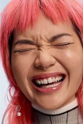 Close-up portrait of a smiling person with vibrant pink hair, septum piercing, and silver hoop earrings against a neutral background