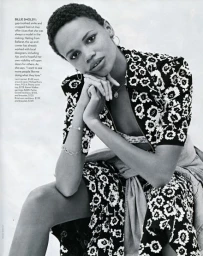 Black-and-white fashion editorial portrait of a model with short hair resting her chin on her hands, wearing a patterned floral top.