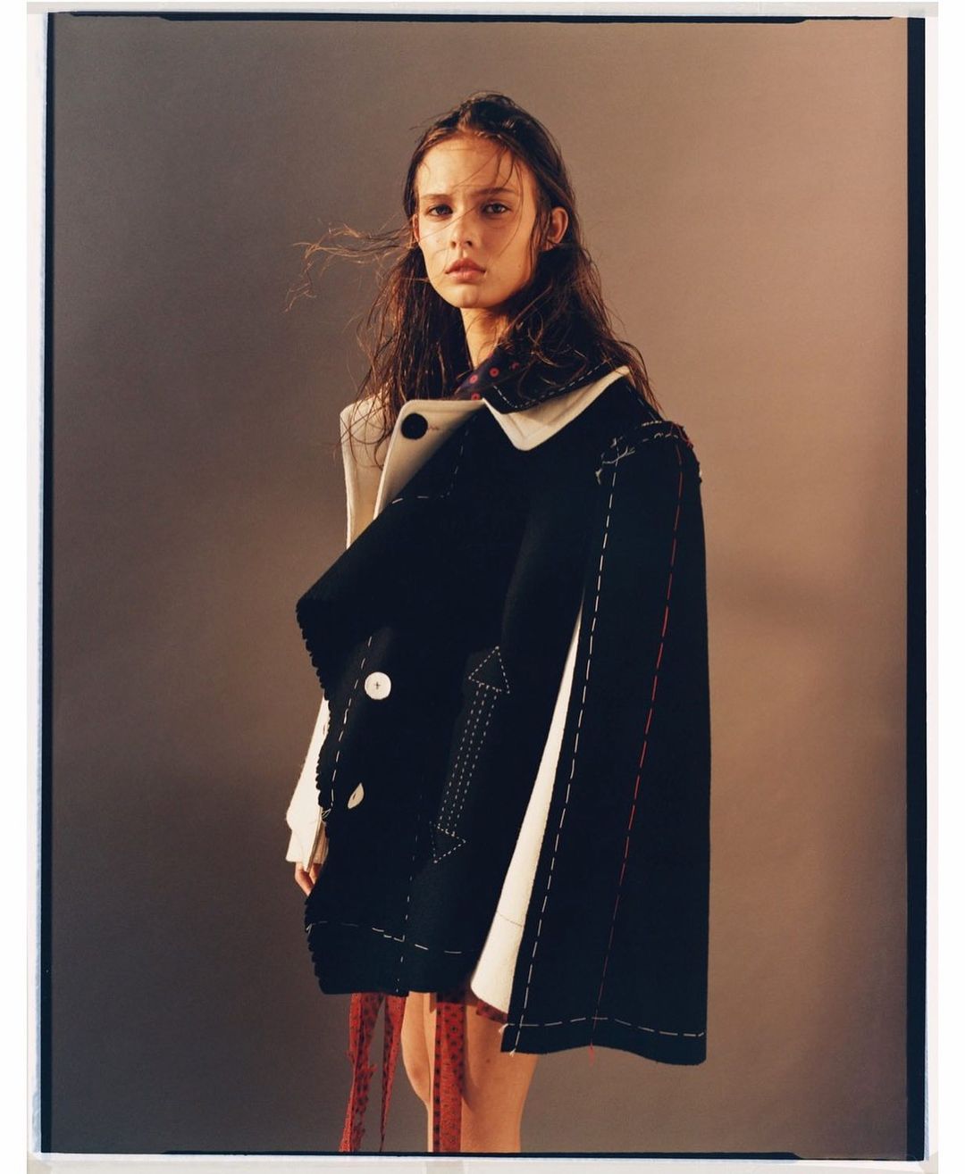 Fashion photography of a female model in a black and white coat against a grey background, studio lighting, and medium framing.