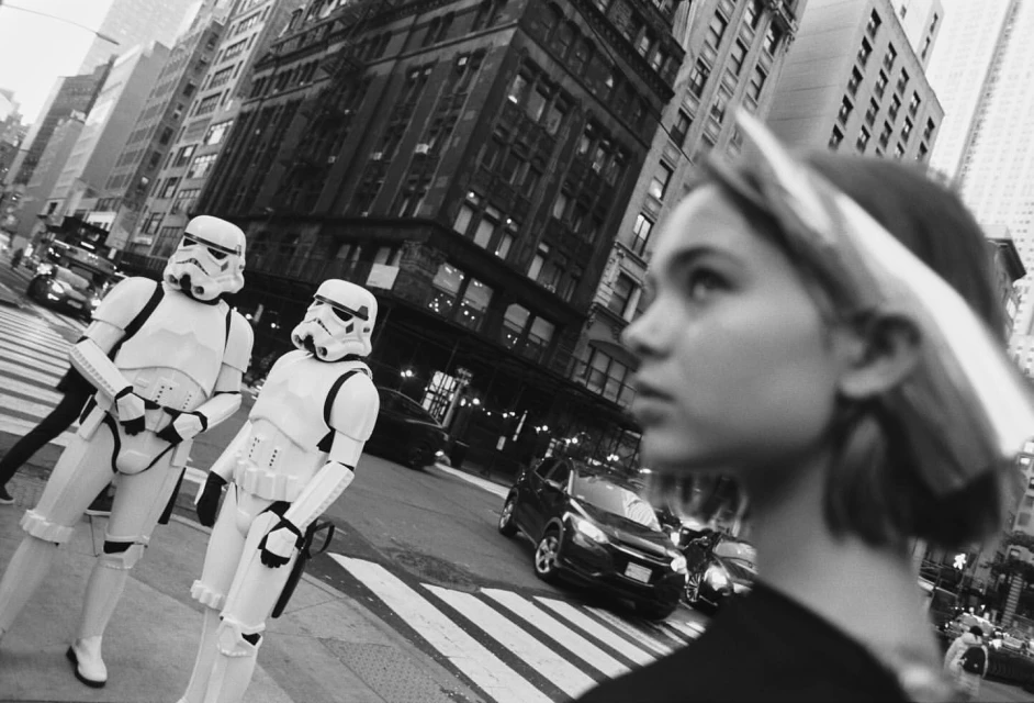 Black and white street view of two Star Wars stormtroopers crossing the street, with a young woman in the foreground.
