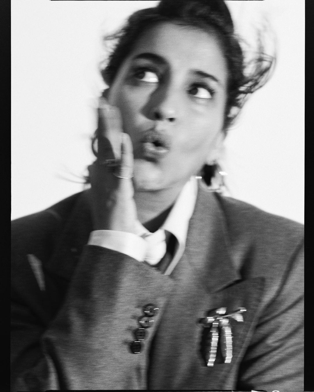 Black and white portrait of a woman in a tailored suit jacket holding her hand to her cheek with a playful expression