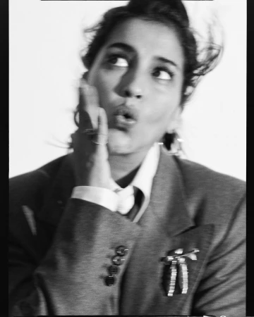 Black and white portrait of a woman in a tailored suit jacket holding her hand to her cheek with a playful expression