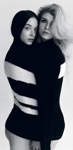 Monochrome studio portrait of two fair-skinned young women embracing, wearing black and white striped sweaters against a white backdrop.