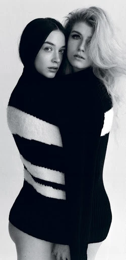 Monochrome studio portrait of two fair-skinned young women embracing, wearing black and white striped sweaters against a white backdrop.