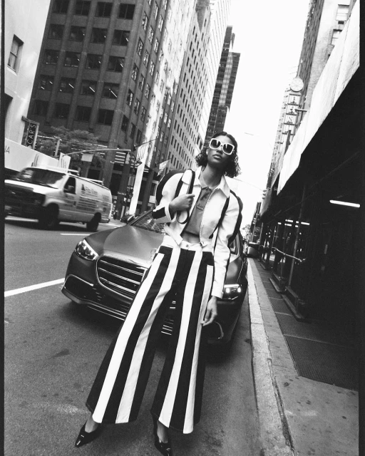Woman in striped pants posing in an urban setting with modern buildings, car, and black and white style, creating a fashion editorial shot.