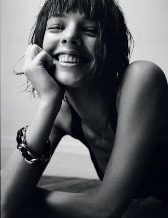 Black and white portrait of a smiling young woman with short hair wearing a chain bracelet and resting her chin on her hand.