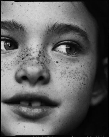Close-up monochrome portrait of a child with prominent freckles and dark eyes by Matteo Montanari.