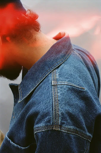 Close up of a male model wearing a denim jacket. The image has a dreamy aesthetic and a strong, warm light source.