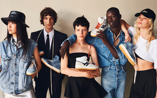 Group of five fashion models showcasing sneakers; diverse ensemble with various denim, black and white clothing, and hats in a studio setting.