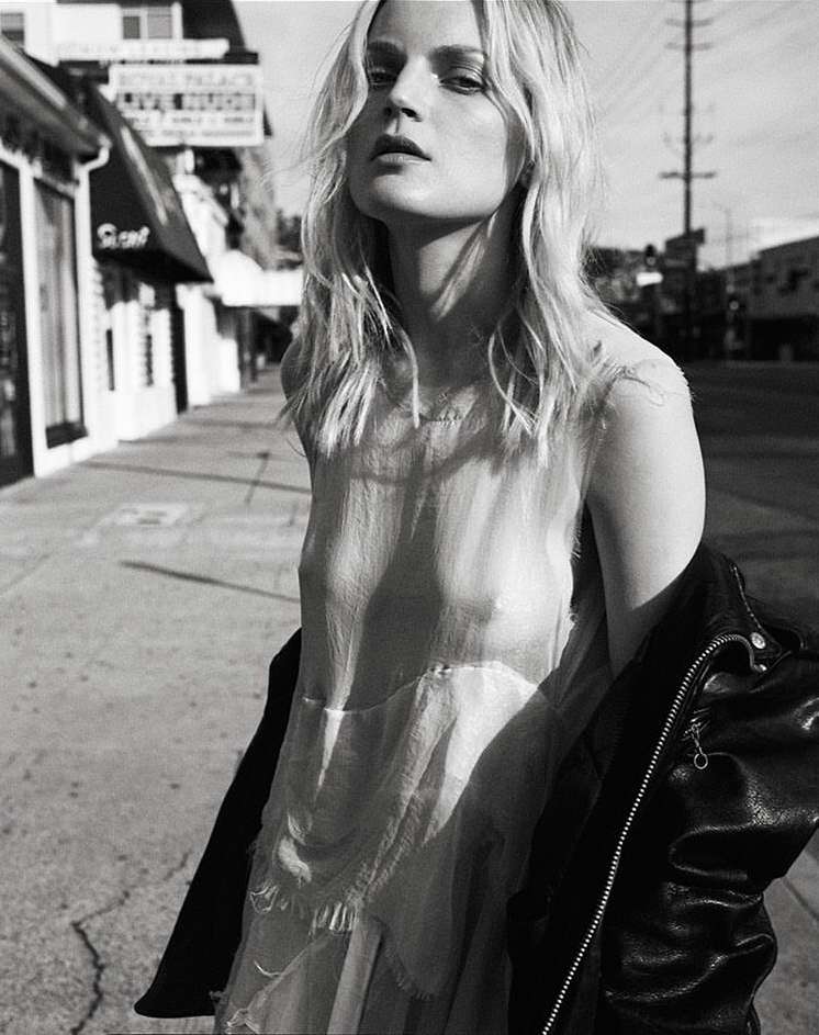 Black and white portrait of a woman in a dress standing outside on a city street with a leather jacket over her shoulder.