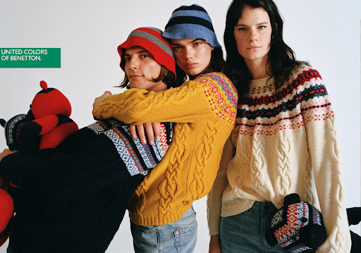 Three fashion models in patterned knit sweaters and hats pose in a studio with teddy bear props, showcasing a modern fashion editorial.