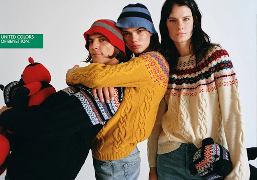 Three fashion models in patterned knit sweaters and hats pose in a studio with teddy bear props, showcasing a modern fashion editorial.
