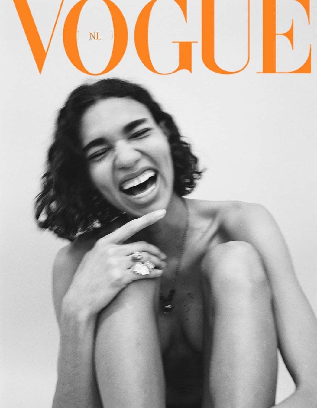 Vogue NL cover featuring a smiling woman with curly hair, jewelry, and a black-and-white edit against a light gray backdrop.