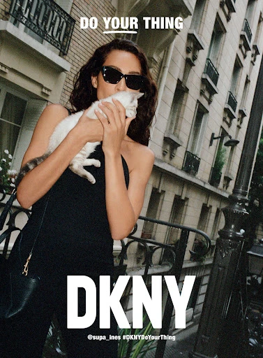 Woman in black halter top holds white cat in an outdoor urban setting with DKNY logo and 'Do Your Thing' tagline.