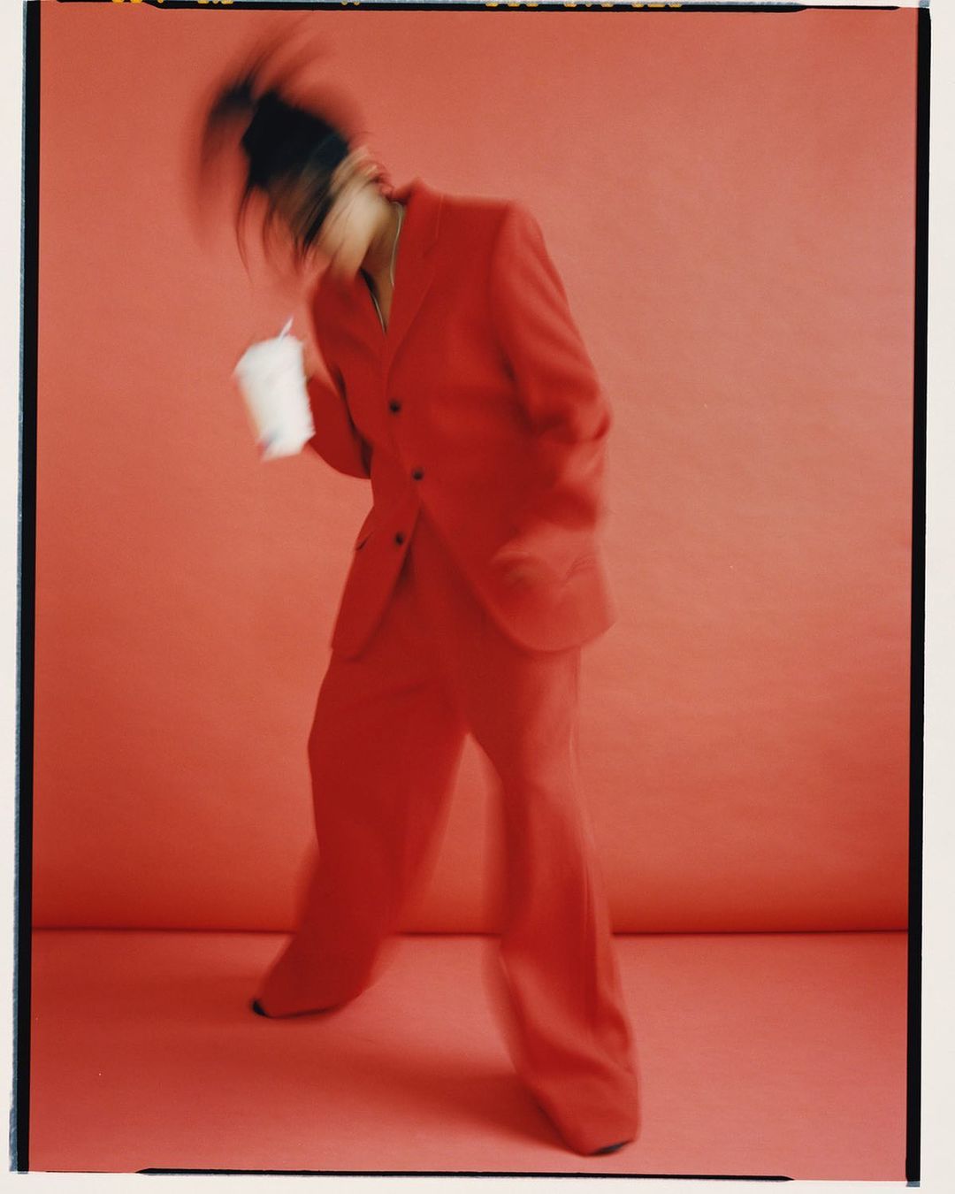 Person in a red suit dances with a drink on a red studio background, motion blur, full body view, fashion photography.