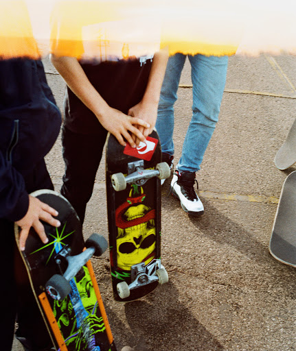 Group of young people with skateboards on an outdoor surface, showcasing urban youth culture and casual street style in bright sunlight.