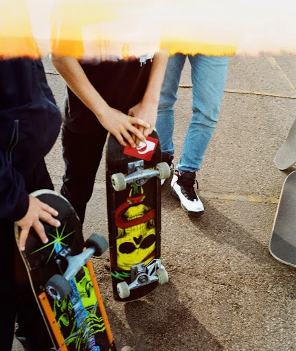 Group of young people with skateboards on an outdoor surface, showcasing urban youth culture and casual street style in bright sunlight.