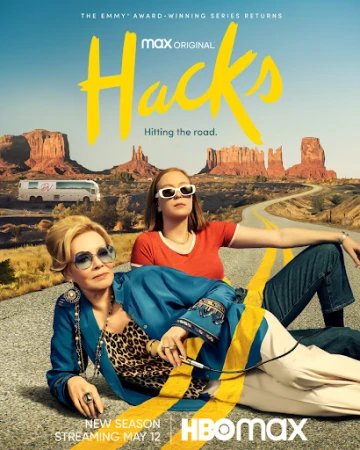Two adult women lying on a highway with desert landscape in the background. One woman is wearing sunglasses, blue top and leopard print top.